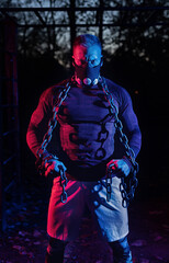 Young tough muscular man with training mask and workout chains around his torso giving you a staredown scary look as he takes a break from a hard strength training in the park