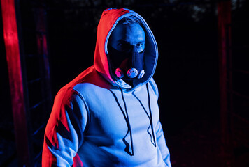Close up of a strong dangerous man with a hoodie and running respiratory boosting mask at dusk