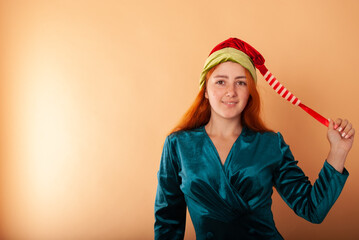 Naklejka premium a red-haired girl in a Santa Claus hat for the new year and giving birth on a beige background for advertising with space for text