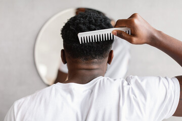 Naklejka premium Black Man Combing Hair Standing Near Mirror In Bathroom, Back-View