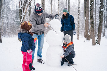 Children play outdoors in snow. Outdoor fun for family Christmas vacation. Two little kid boy and girl in funny hats playing outdoors. Happy siblings having fun with snowman