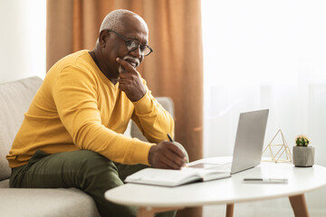 Mature Black Male Freelancer Using Laptop Taking Notes Working Indoors