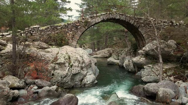 Drone view pulling back from an ancient Genoese bridge over the clear water of the fast flowing Tartagine river in the Balagne region of Corsica