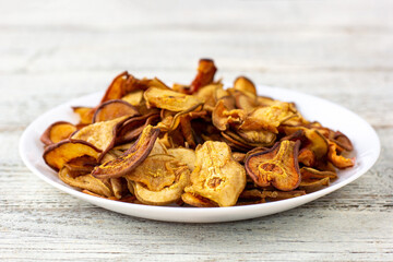 A pile of dried pears in slices on a white plate on wooden background. Dried fruit chips. Healthy food
