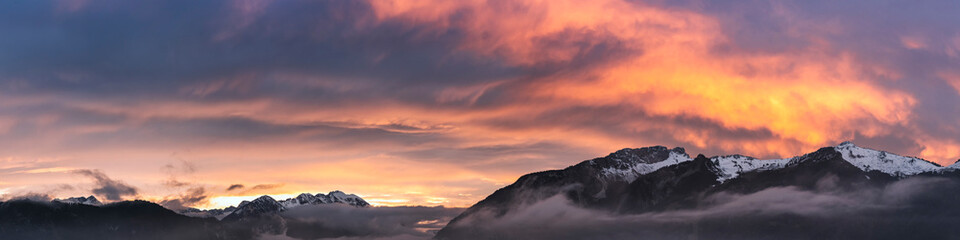fog covered hahnenkamm mountain range with dramatic orange-red sky at sunset in late autumn