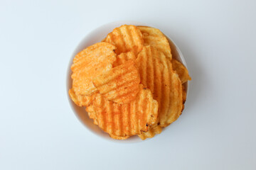 Wavy potato chips, with red powder seasoning, on a small plate. Isolated on white background. Top view or flat lay