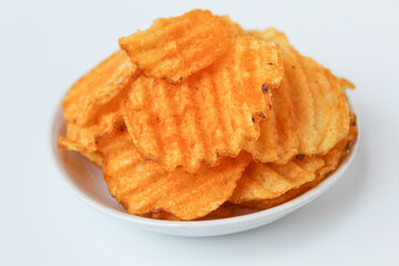 Wavy potato chips, with red powder seasoning, on a small plate. Isolated on white background.