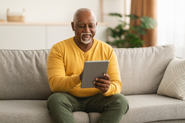 Senior Black Man Using Tablet Browsing Internet Sitting At Home