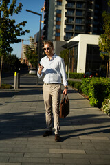 Fototapeta premium Young stylish businessman with e-scooter. Portrait of handsome man looking at wristwatch