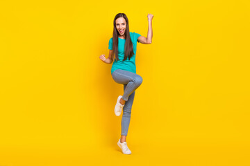 Fototapeta na wymiar Photo of astonished glad lady raise fists rejoice win wear teal t-shirt jeans shoes isolated yellow color background