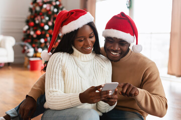 Happy festive black family using cellphone choosing gifts on Xmas