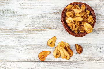 A pile of dried slices of pears in wicker basket on white wooden background. Dried fruit chips. Healthy food