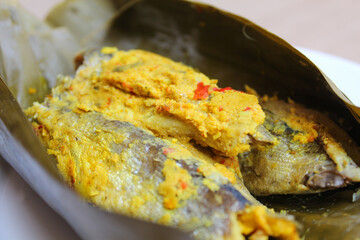 Pepes ikan, or steamed fish with herbs then wrapped in banana leaf. Indonesia traditional food. Wooden background.