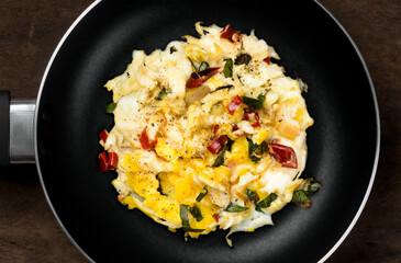 scrambled eggs on a black pan over dark wooden table top, cooked with onion, red chilies, curry leaves,flat lay, top view