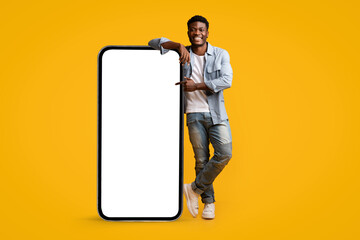 Stylish black guy standing by huge smartphone with blank screen