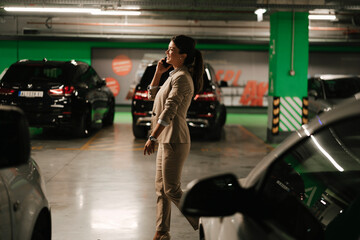 Fototapeta na wymiar Businesswoman in suit unlocking car on parking. Beautiful woman talking to the phone.