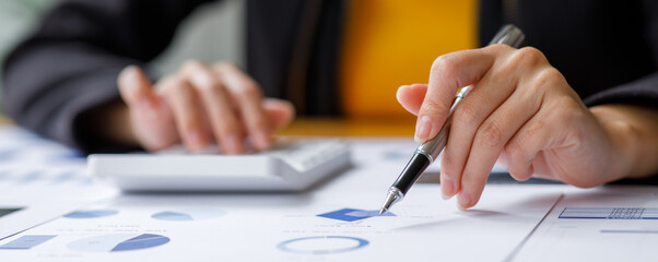 Close up a Business woman using calculator and laptop for doing math finance on a wooden desk, tax, accounting, statistics, and analytical research concept