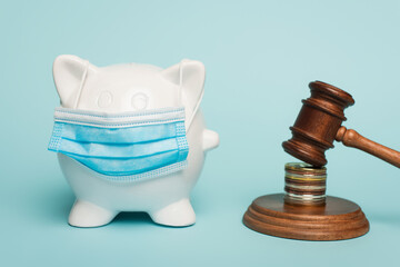 piggy bank in medical mask near gavel with coins on blue, anti-corruption concept