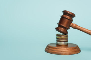 wooden gavel on stacked golden and silver coins on blue, anti-corruption concept