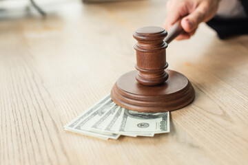 partial view of judge holding wooden gavel near dollar banknotes on desk, anti-corruption concept