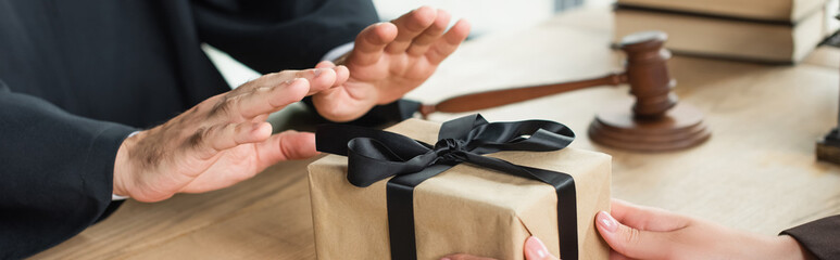 partial view of judge showing refuse gesture near woman with gift box, anti-corruption concept,...