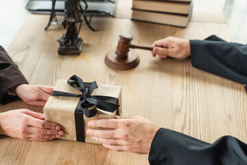 partial view of lawyer holding gavel while taking gift box from client, anti-corruption concept