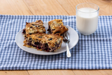 Homemade delicious sliced Apple Blueberry Pie on a white plate and glass of milk on a wooden table with fork and a blue cloth