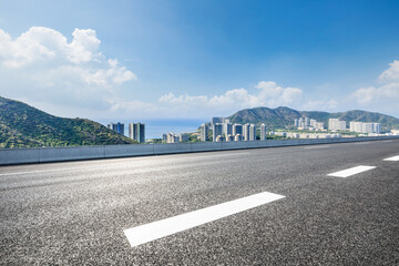 Naklejka premium Asphalt road and modern city commercial buildings with skyline by the sea