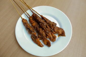 Chicken satay covered by peanut sauce, with bamboo skewers. Indonesian traditional food. On a white plate. Isolated on white background