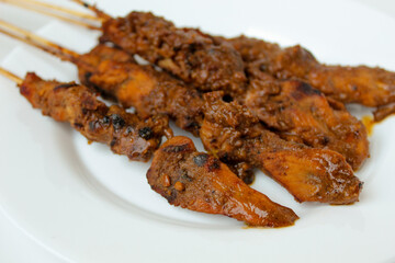 Chicken satay covered by peanut sauce, with bamboo skewers. Indonesian traditional food. On a white plate