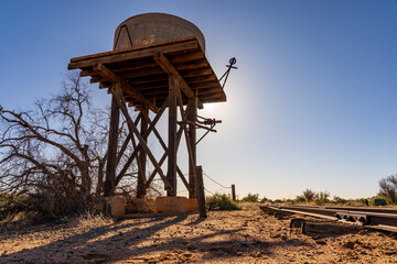 Looking up at a rustic wooden tank stand with an old water tank on top and the Sun behind