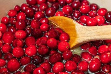 Close up of wooden spoon stirring cranberries in sugar syrup for cranberry sauce at Tnanksgiving