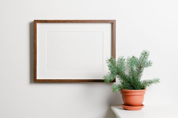 Landscape frame mockup with copy space for artwork, photo or print presentation. White wall interior with christmas tree in terracotta pot.