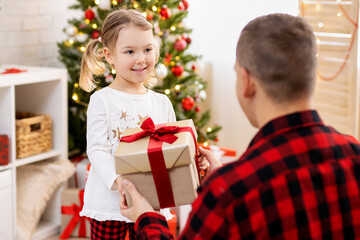 Father giving a present to his happy daughter in Christmas decorated room