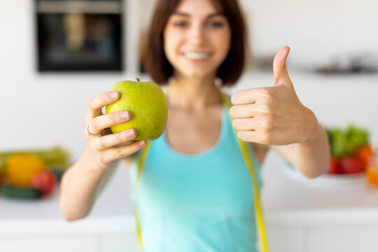 Dieting concept. Fit woman holding apple and showing thumb up, recommending healthy eating, selective focus