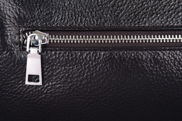 Steel zipper folded on the details or pocket of a black leather jacket or bag as a background.The...