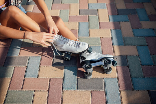 Anonymous woman tying roller skates on street