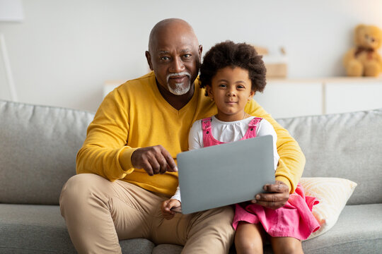 Cheerful black little kid and grandpa surfing in internet or play an online game, watch cartoon on laptop