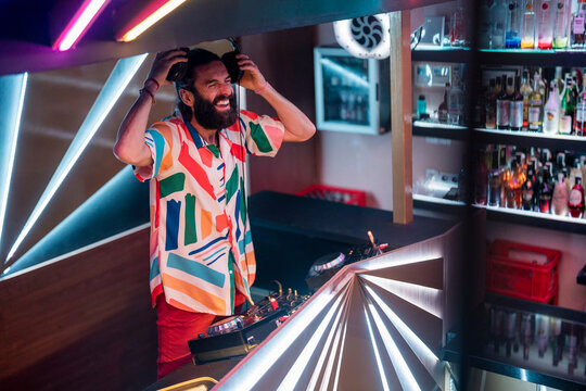 Joyful young disc jockey laughing during party in club