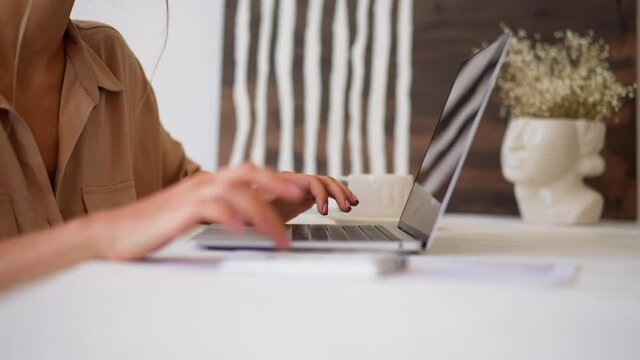 Woman in beige shirt makes calculations on numeric keypad comparing with data on laptop screen at white desk in office room closeup slow motion