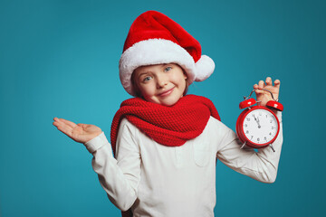 Little kid in christmas hat and red scarf, holding red alarm clock while shrugging her shoulders, saying: who cares, so what.