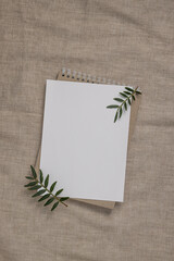 Summer wedding stationery mock-up scene. Blank greeting card, craft paper envelope and green branches on linen textile background.