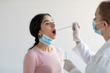 European doctor doing covid-19 pcr test for young indian woman on gray wall background in clinic