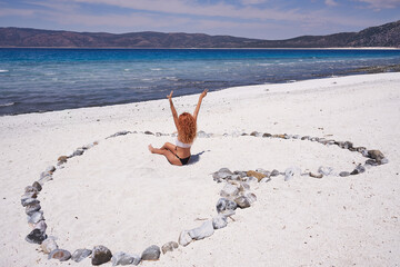 Happy woman on the white sand beach sitting inside big heart. Happy Valentines day on the beach - concept holiday.Heart shape on a beach.Valentine's Day.Honeymoon beach