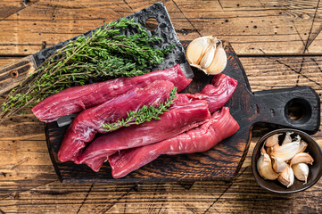 Raw lamb tenderloin Fillet Meat on butcher board with meat cleaver. wooden background. Top view