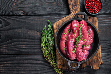 Raw mutton tenderloin Fillet Meat, lamb sirloin in rustic pan with thyme. Black wooden background. Top view. Copy space