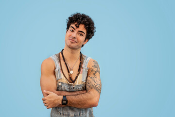Photo of handsome stylish spanish man with tattoos wearing trendy denim dungarees and necklaces,...
