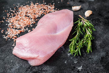 Raw Poultry turkey breast fillet meat on a butcher table with rosemary and salt. Black background. Top View