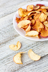 A pile of dried apples in slices on a white plate on wooden background. Dried fruit chips. Healthy food