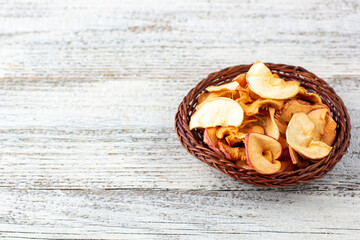 A pile of dried slices of apples in wicker basket on white wooden background. Dried fruit chips. Healthy food